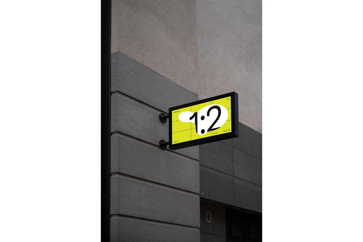 Bright yellow sign mockup with '1:2' graphic, mounted on a grey building corner.