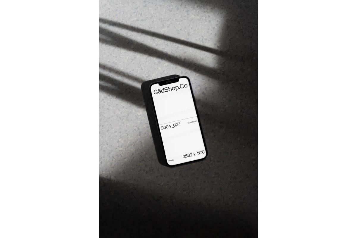 Smartphone screen mockup under dramatic shadow patterns on a textured surface.