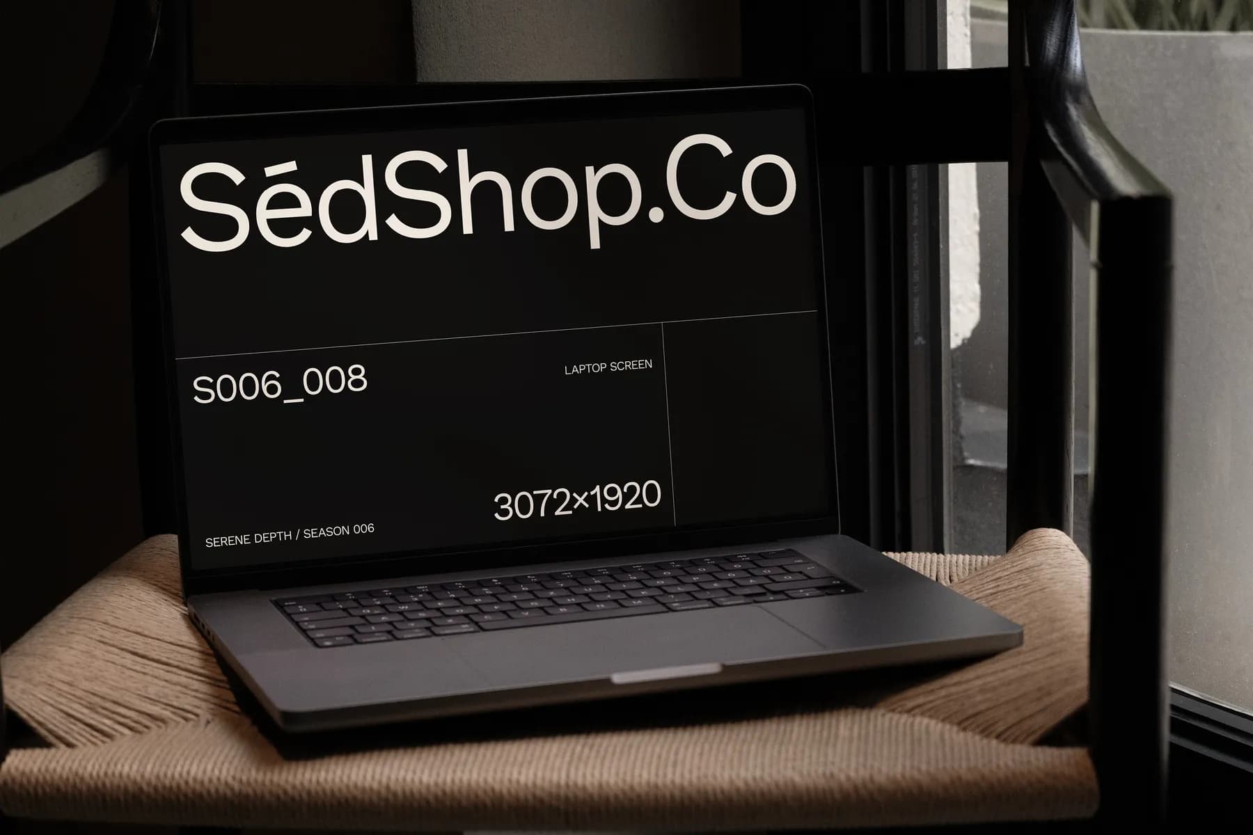 Close-up view of a laptop screen mockup displaying text and screen resolution, with the laptop resting on a chair by a window.