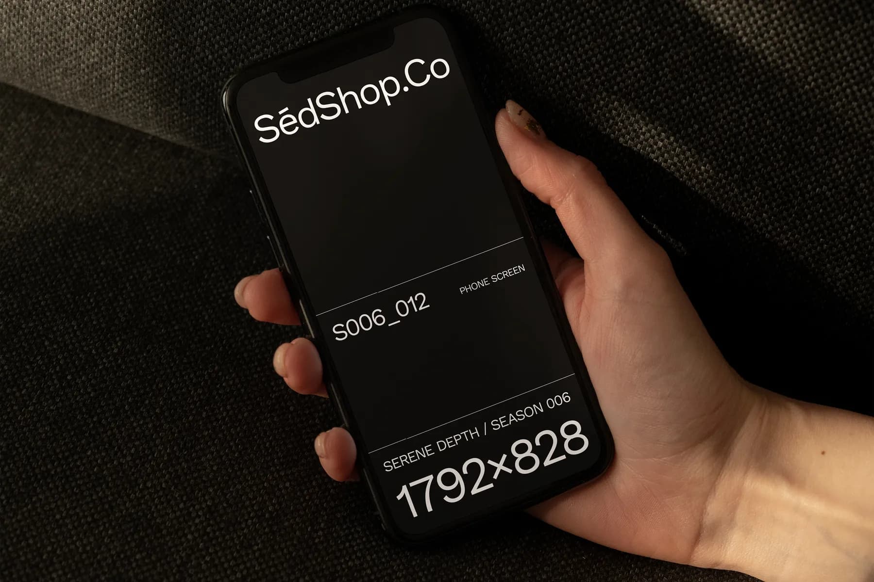 Close-up view of a phone screen mockup with text and design details, held by a hand over a textured fabric surface.