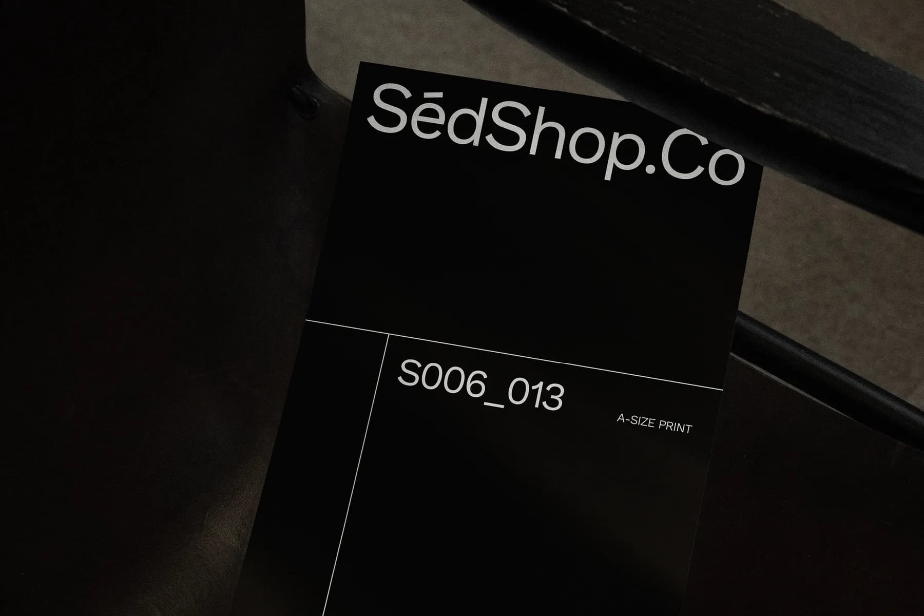 Close-up of an A4 poster mockup on a dark chair, highlighting the SédShop.Co branding with a dark color scheme and minimalist layout.