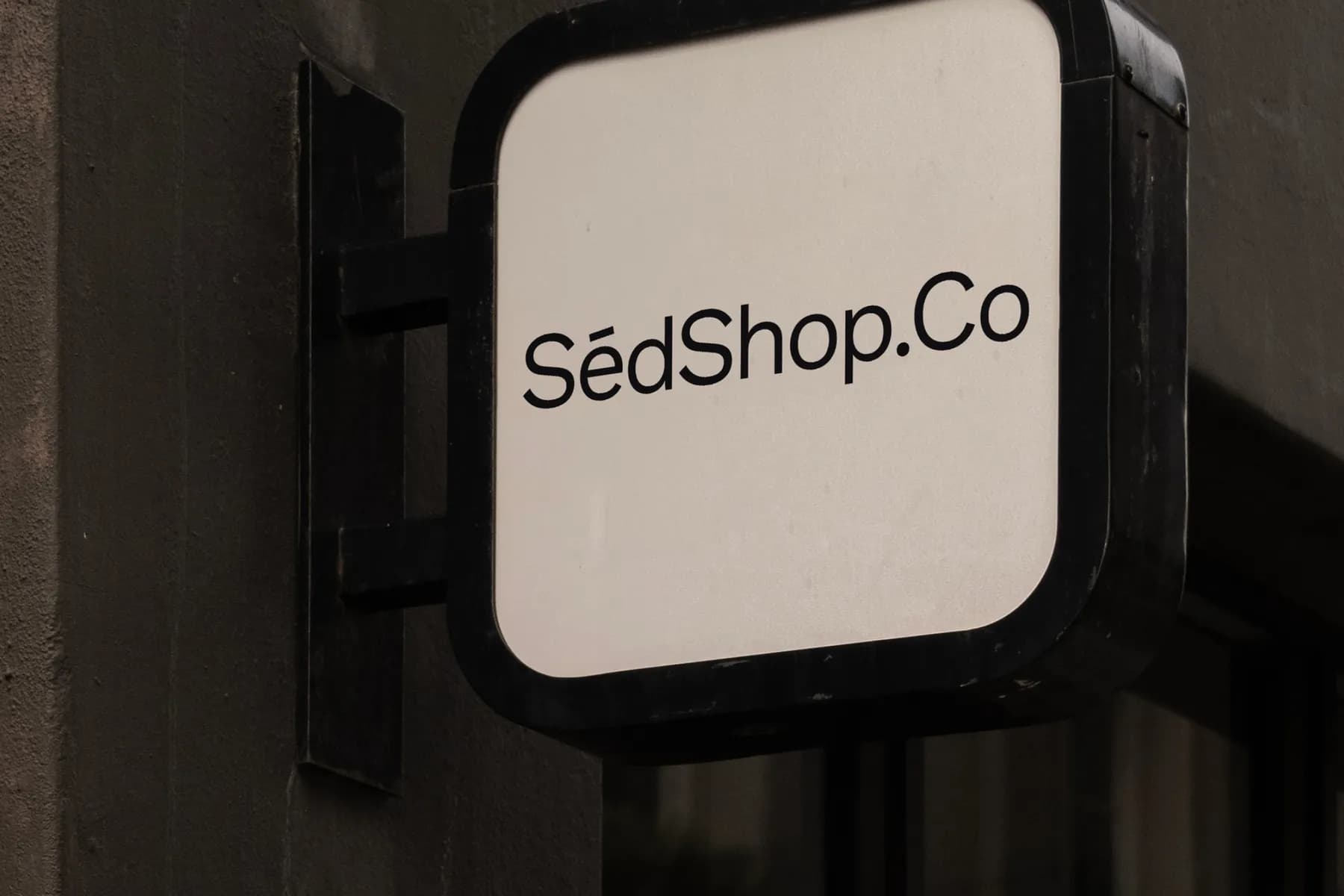 Close-up view of a sign mockup attached to a building, displaying 'SédShop.Co' text, ideal for showcasing branding in an urban environment.