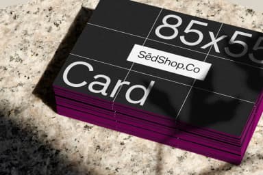 Close-up mockup of business cards with a black front and magenta edges, stacked on a textured stone surface.