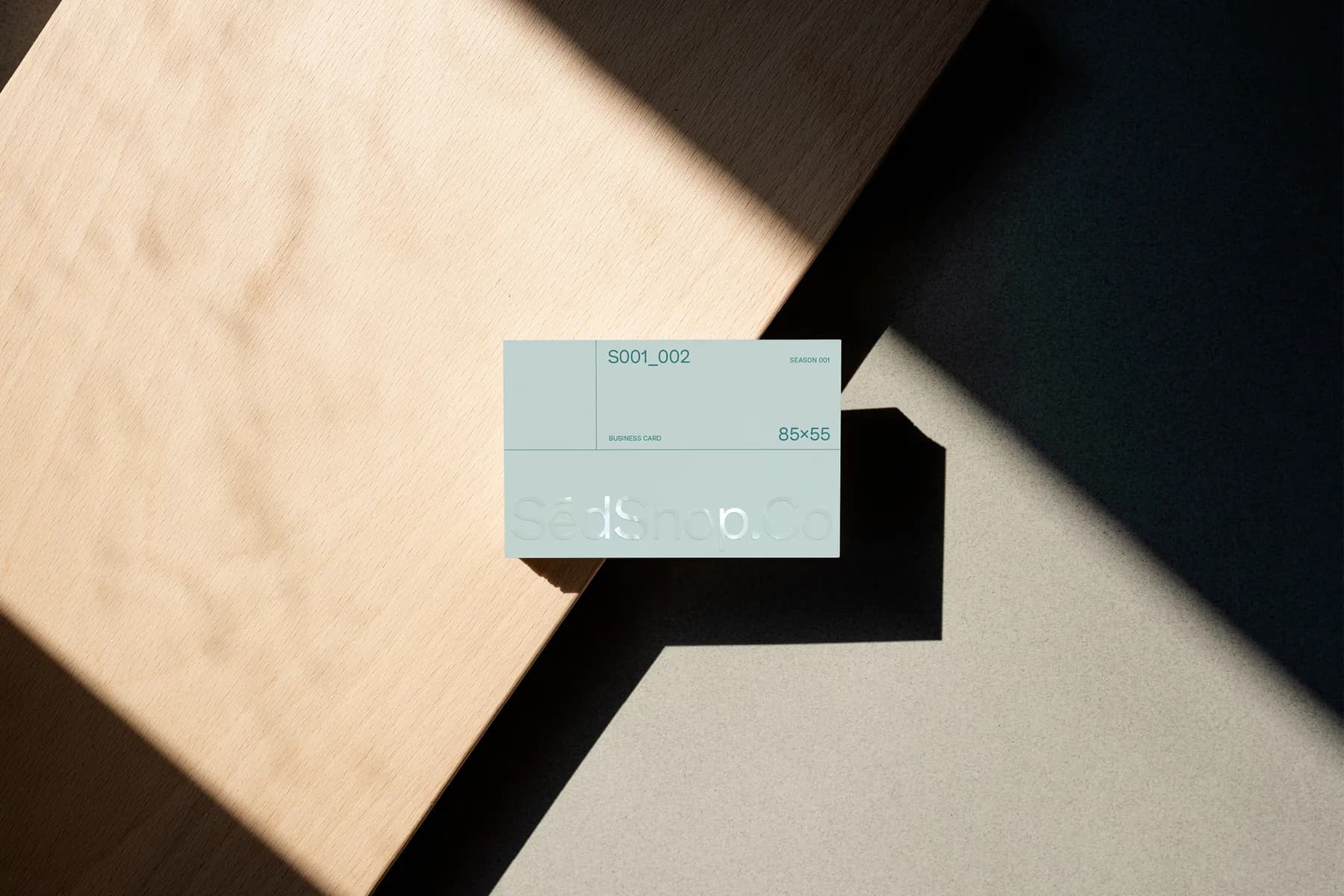 Mockup of a mint green business card on a wooden surface, with shadows cast by the card’s edge.