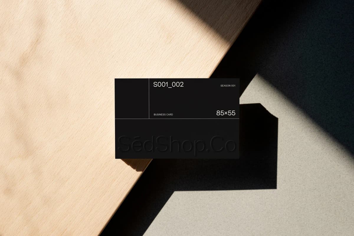 Black business card mockup on a wooden surface with embossed text, casting shadows on the background.