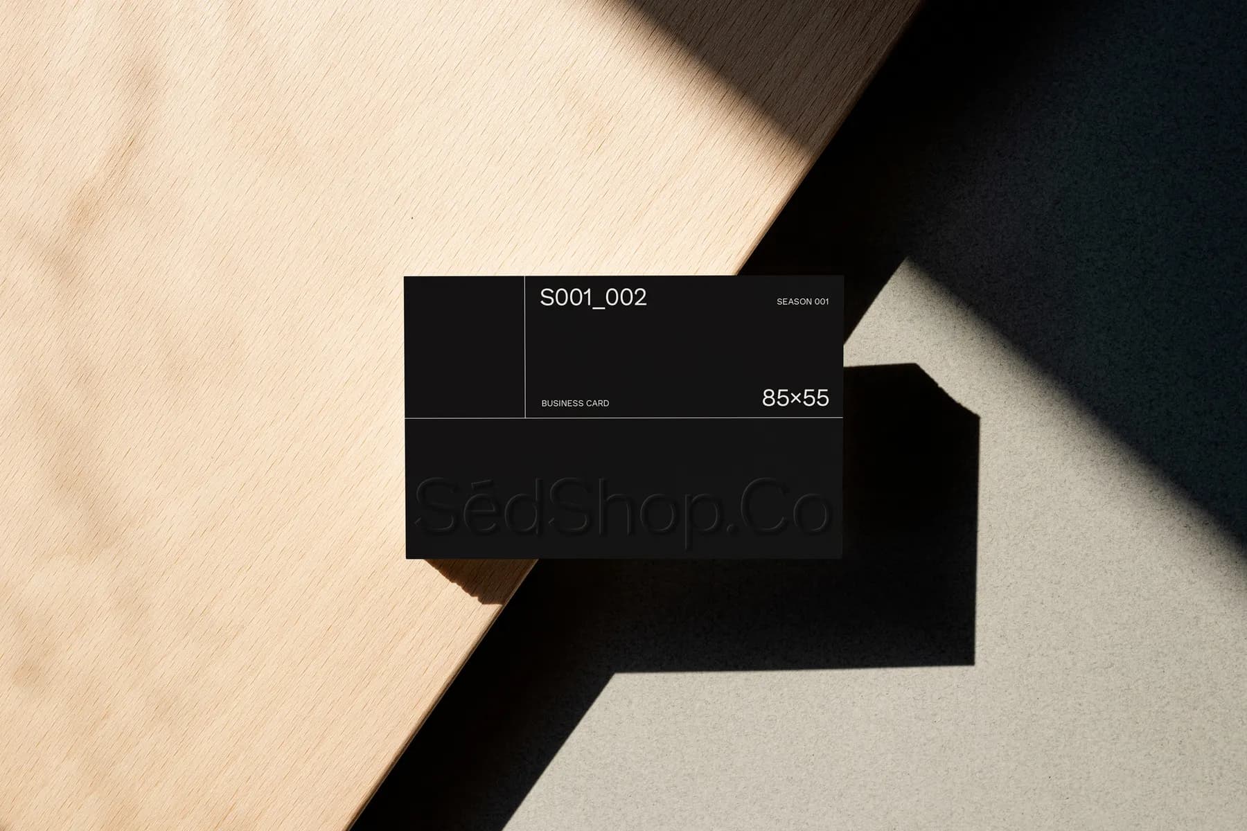 Black business card mockup on a wooden surface with embossed text, casting shadows on the background.