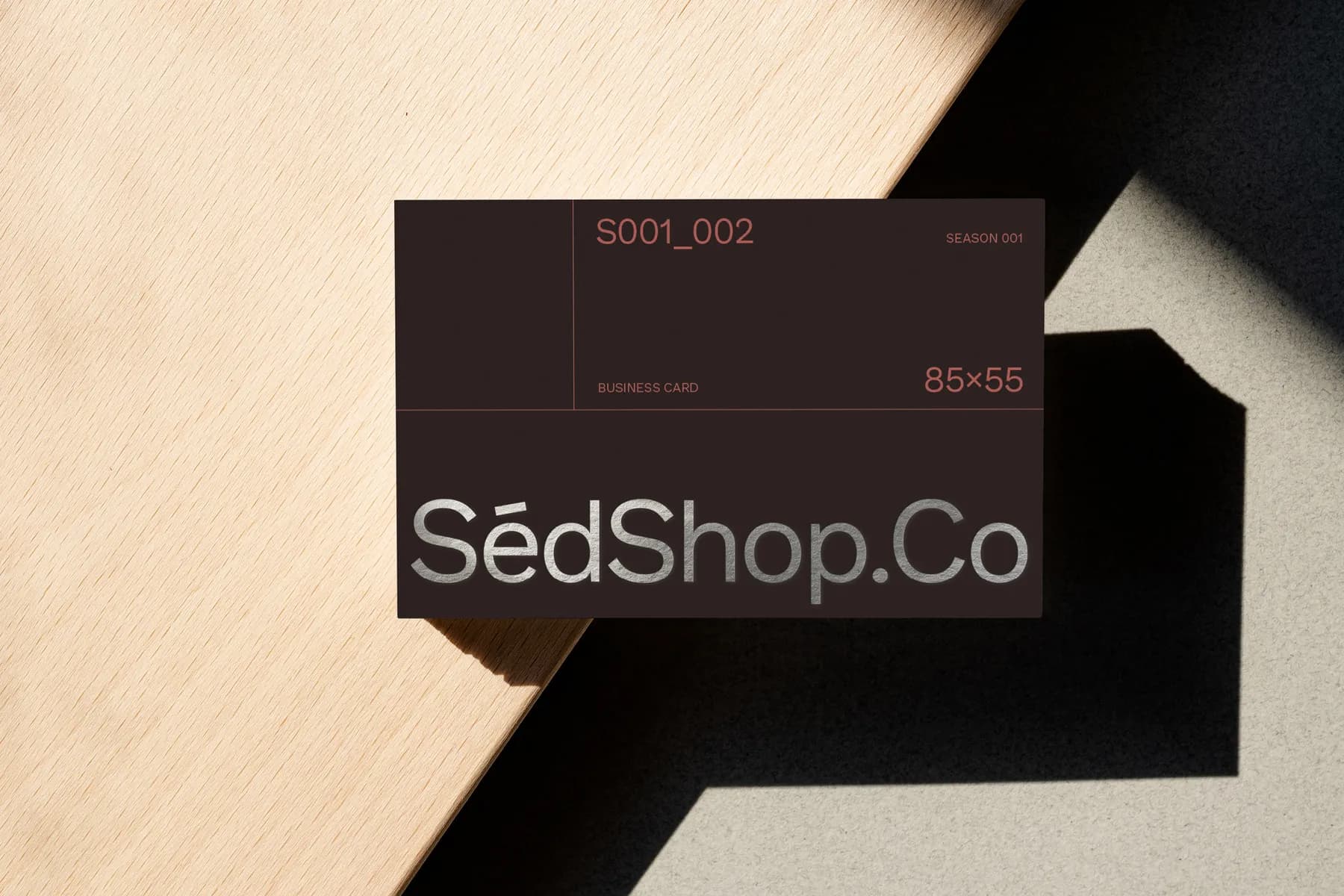 Business card mockup featuring a metallic foil effect on a dark background, positioned on a shadowed surface.